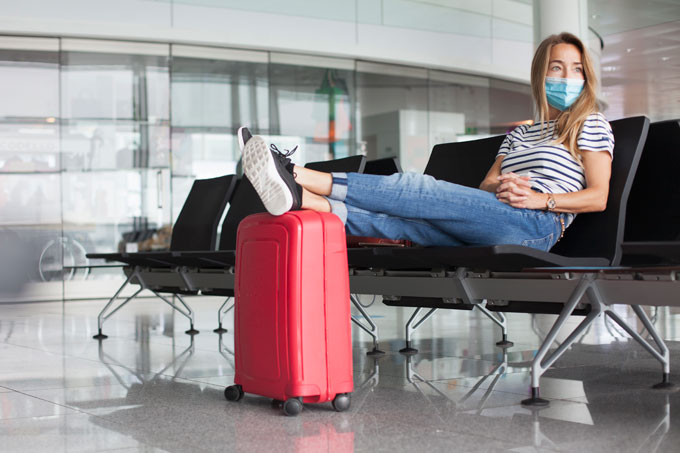 Moça jovem no aeroporto, sentada, com os pés sobre uma mala vermelha