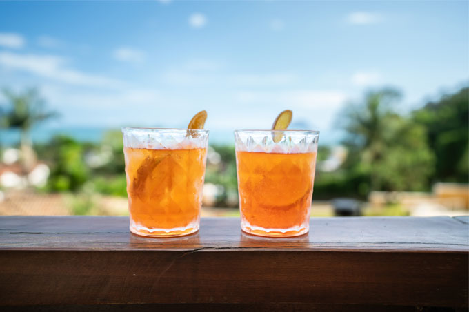 Dois copos com drinques de Aperol em balcão com cenário tropical ao fundo