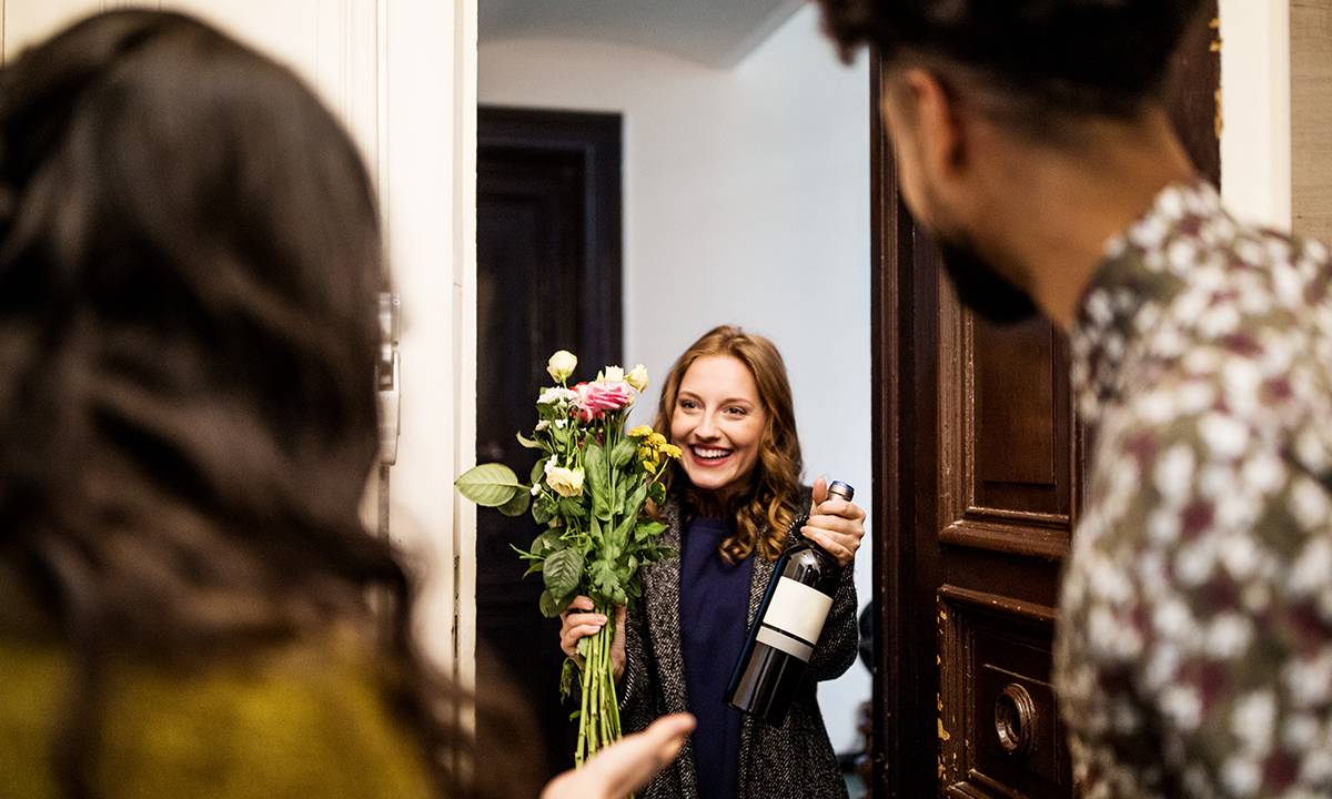 mulher na porta de casa dos amigos com flores e presentes