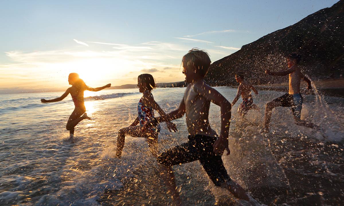 crianças correndo na praia ao por do sol