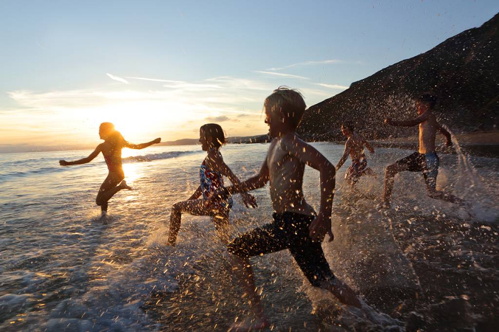 crianças correndo na praia ao por do sol